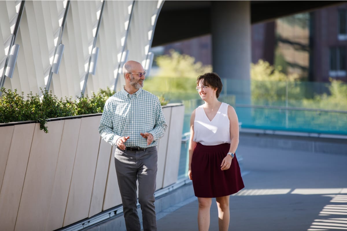 Two people are walking beside a building and discussing with each other